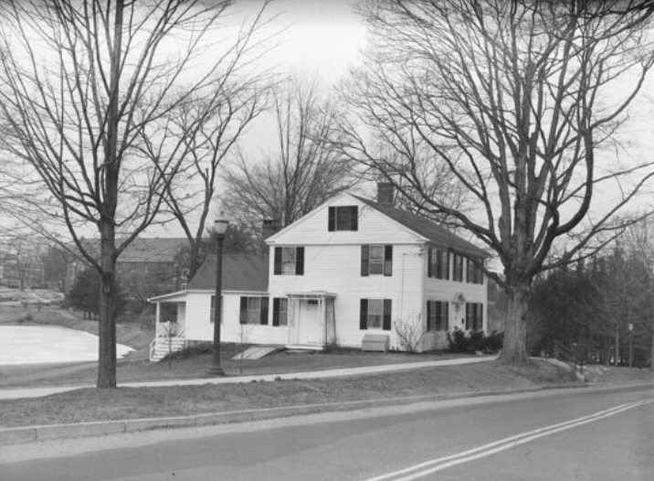 Black-and-white photo of a white three-story house surrounded by bare trees.