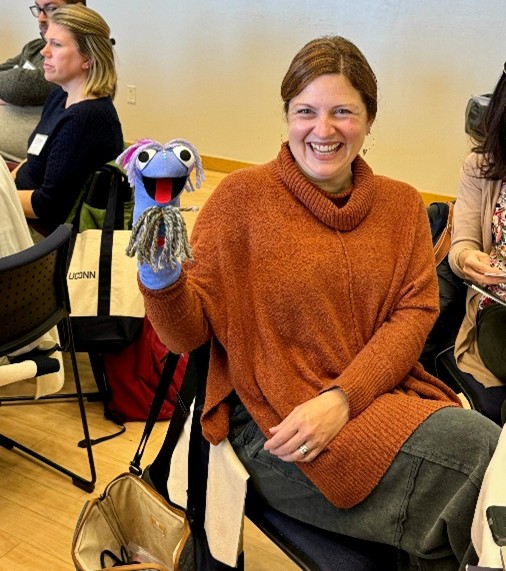 A woman holds up a purple sock puppet.