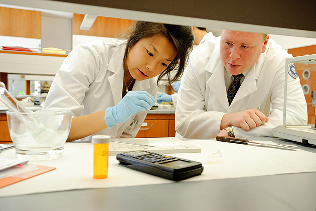 Andrea Kam, left, hand fill capsules at the dosage forms lab in the Pharmacy/Biology Building as Zachary Binkowski, a fourth year student looks on.