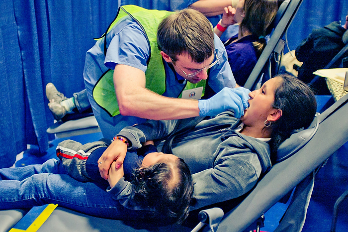 A patient holds a child on her lap while receiving treatment from second-year dental student Brendan Dolan at the 2012 Connecticut Misson of Mercy on on March 26, 2012. (Photo by Xing Zhu)