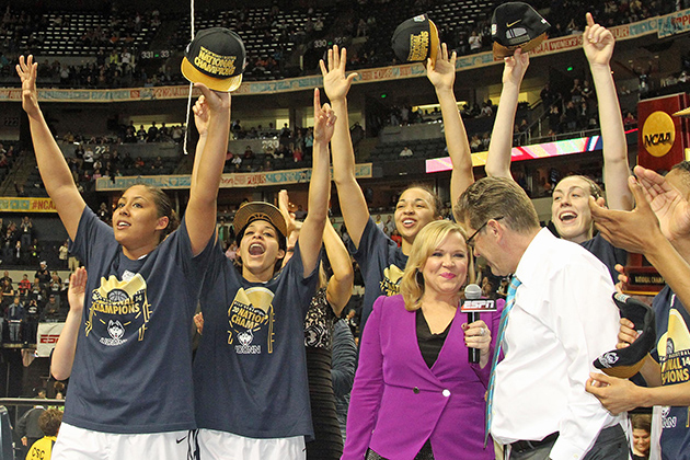 From left Kaleena Mosqueda-Lewis '15 (CLAS), Bria Hartley '14 (CLAS), Kiah Stokes '15 (CLAS), and Breanna Stewart '16 (CLAS) celebrate the team's championship win in Nashville, Tenn., while head coach Geno Auriemma is interviewed for ESPN. (Bob Stowell '70 (CLAS) for UConn)