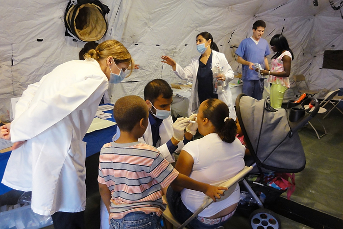 Urban Service Track alumna, Dr. Jennifer Jaskolka (standing far left), observes current UST scholar and third-year dental student, Himank Gupta, performing a dental exam during a free health clinic. (Photo provided by Petra Clark-Dufner)