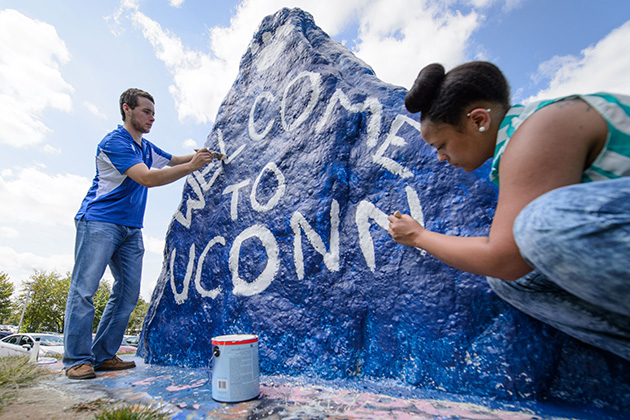 Drew Vandemore '15 (CAHNR), left, and Jasmine Kirkland '16 (CAHNR) paint 'Welcome to UConn' on the rock near the UConn Foundation Building on Aug. 20, 2014. (Peter Morenus/UConn Photo)