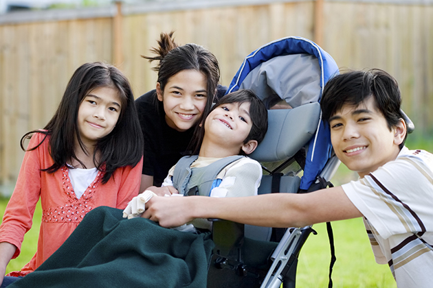 Five year old disabled boy in wheelchair lovingly surrounded by his three older brother and sisters (istock photo)