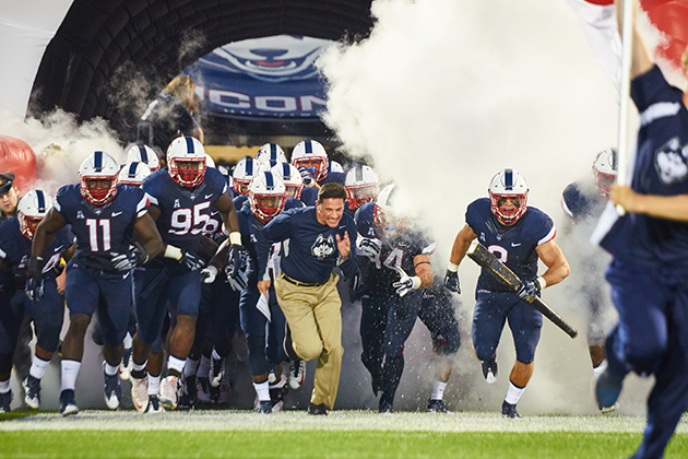 Coach Bob Diaco and the UConn football run onto the field at Pratt & Whitney Stadium on Sept. 3, 2015. (Peter Morenus/UConn Photo)