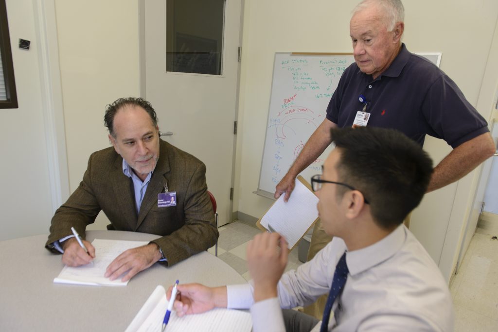 Dr. Thomas Devers (standing) provides biopsies from dozens of colonoscopies a year – and demographic data from about 1,000 colonoscopies a year – to the laboratory of Daniel W. Rosenberg (left). The collaboration has led to several studies that are on track for publication. Allen Mo (right) is first author of a paper that was just accepted by a major scientific journal. (Janine Gelineau/UConn Health Photo)