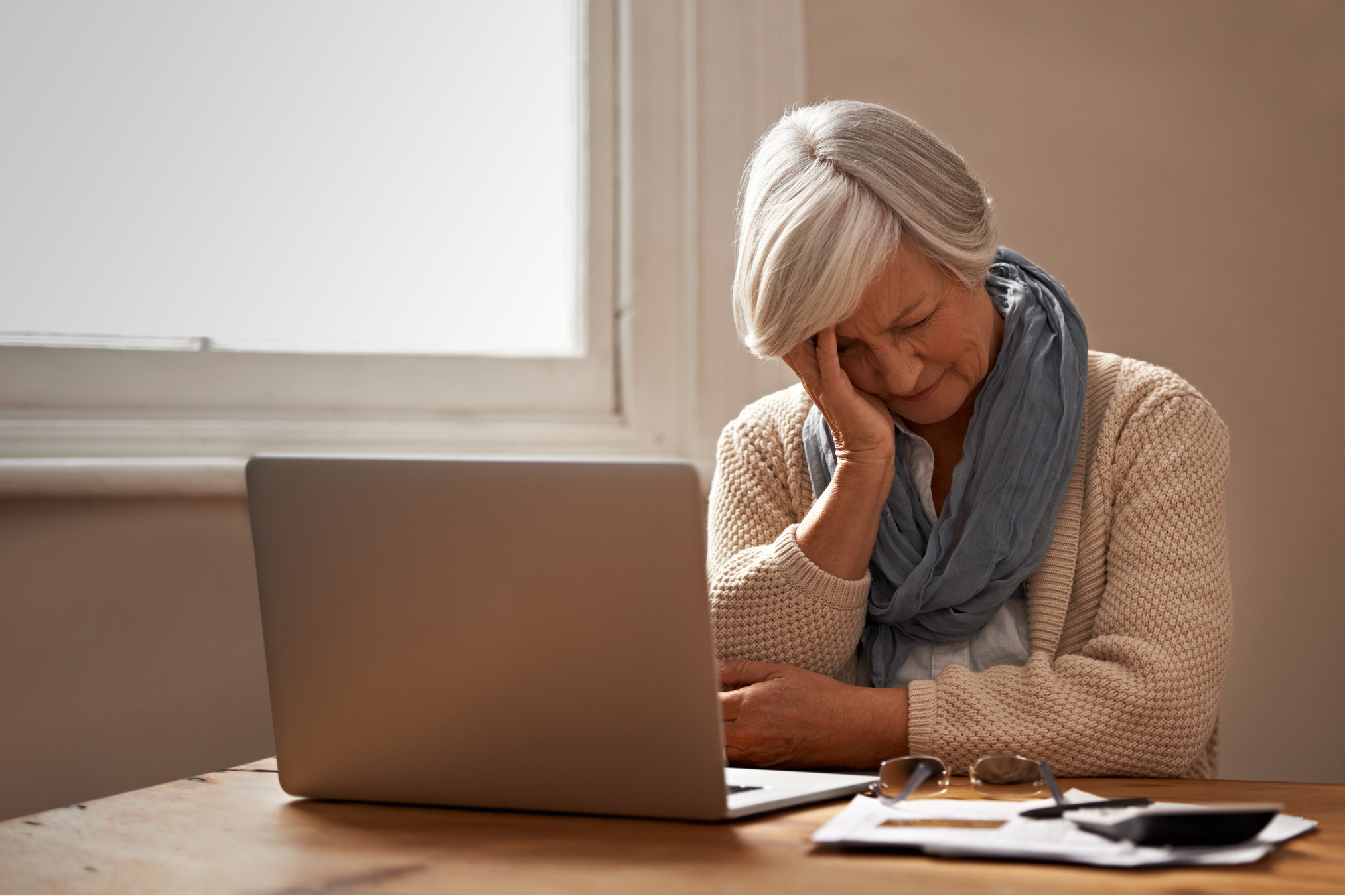 An elderly woman sitting in front of her laptop looking stressed. (PeopleImages via Getty Images)