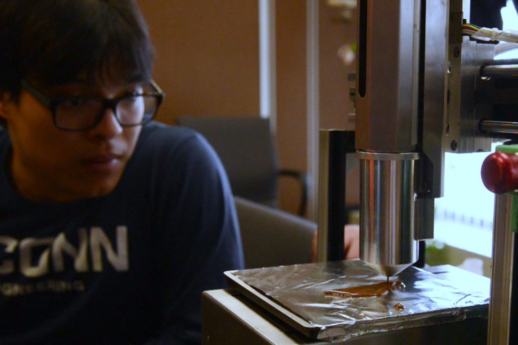 Sam Pradhan '17 (ENG) watches as a 3-D printer creates a Husky dog logo in chocolate. Pradhan is one of a group of UConn engineering students who 3-D printed customized chocolates for their senior design project. (Emily Fitzpatrick '17 (CLAS)/UConn Photo)