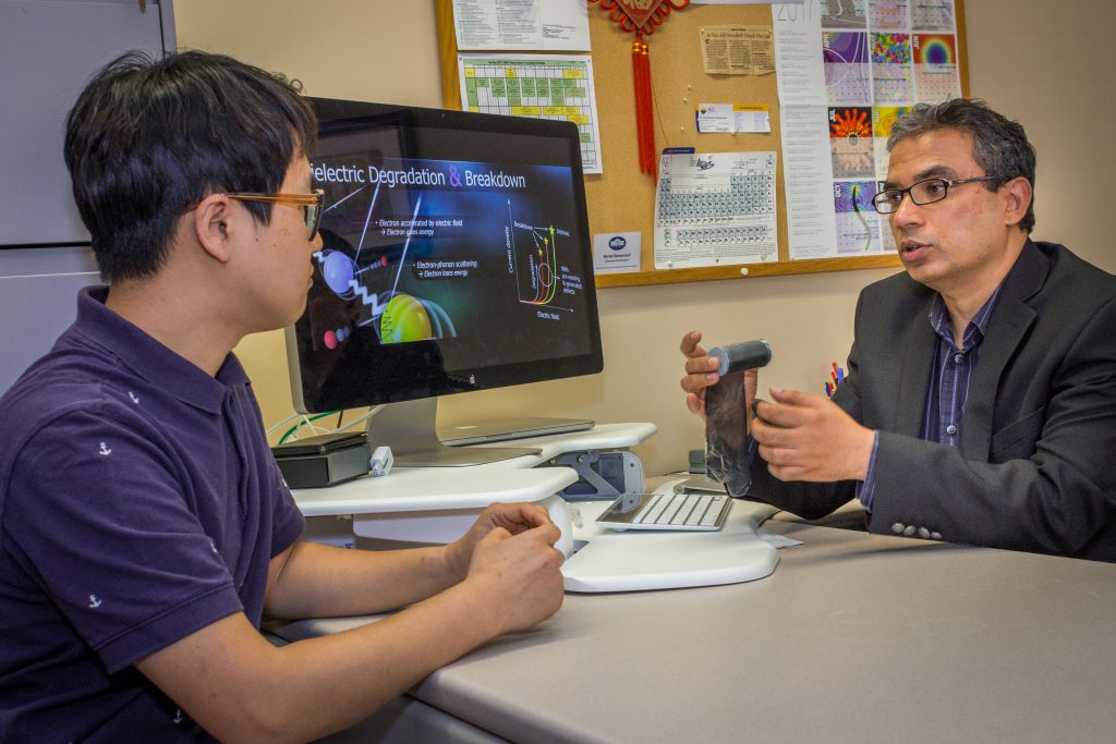 Chiho Kim (left), postdoctChiho Kim (left), postdoctoral fellow, and Rampi Ramprasad, professor of materials science and engineering, discuss a capacitor that Ramprasad is holding. (Christopher LaRosa/UConn Photo)oral fellow and Rampi Ramprasad, professor of Material Science and Engineering, discuss a capacitor that Ramprasad is holding. (Chris LaRosa/UConn Photo)