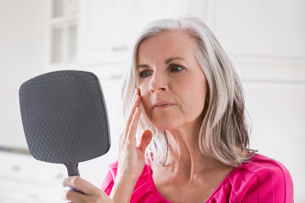 Woman looking at skin in mirror (Shutterstock Photo)