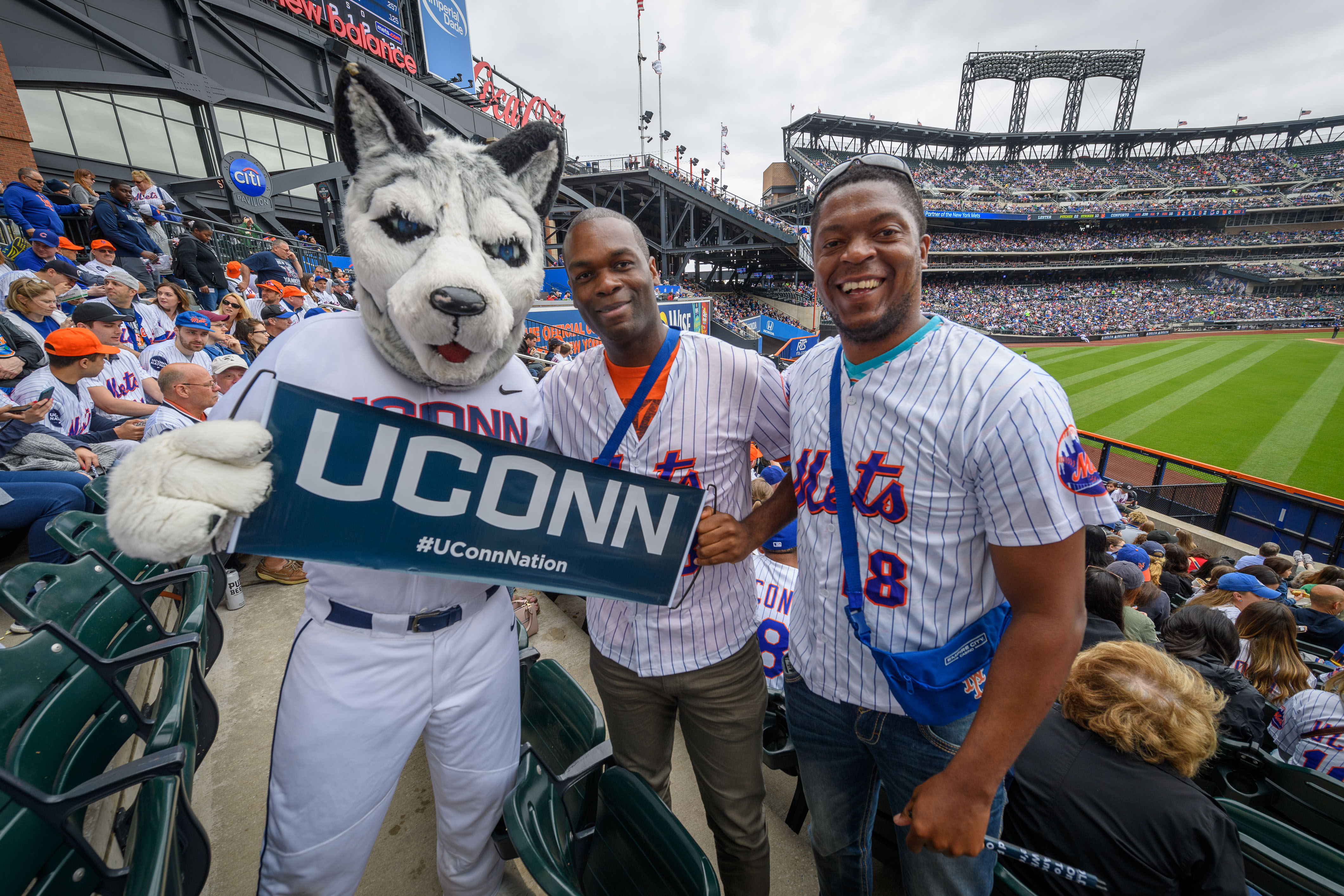 Merlon Pinnock '15 MBA, center, and Oneil McCaulsky, both of Poughkeepsie New York with Jonathan the Husky at a New York Mets baseball game at Citi Field in Queens New York on June 3, 2018. (Peter Morenus/UConn Photo)