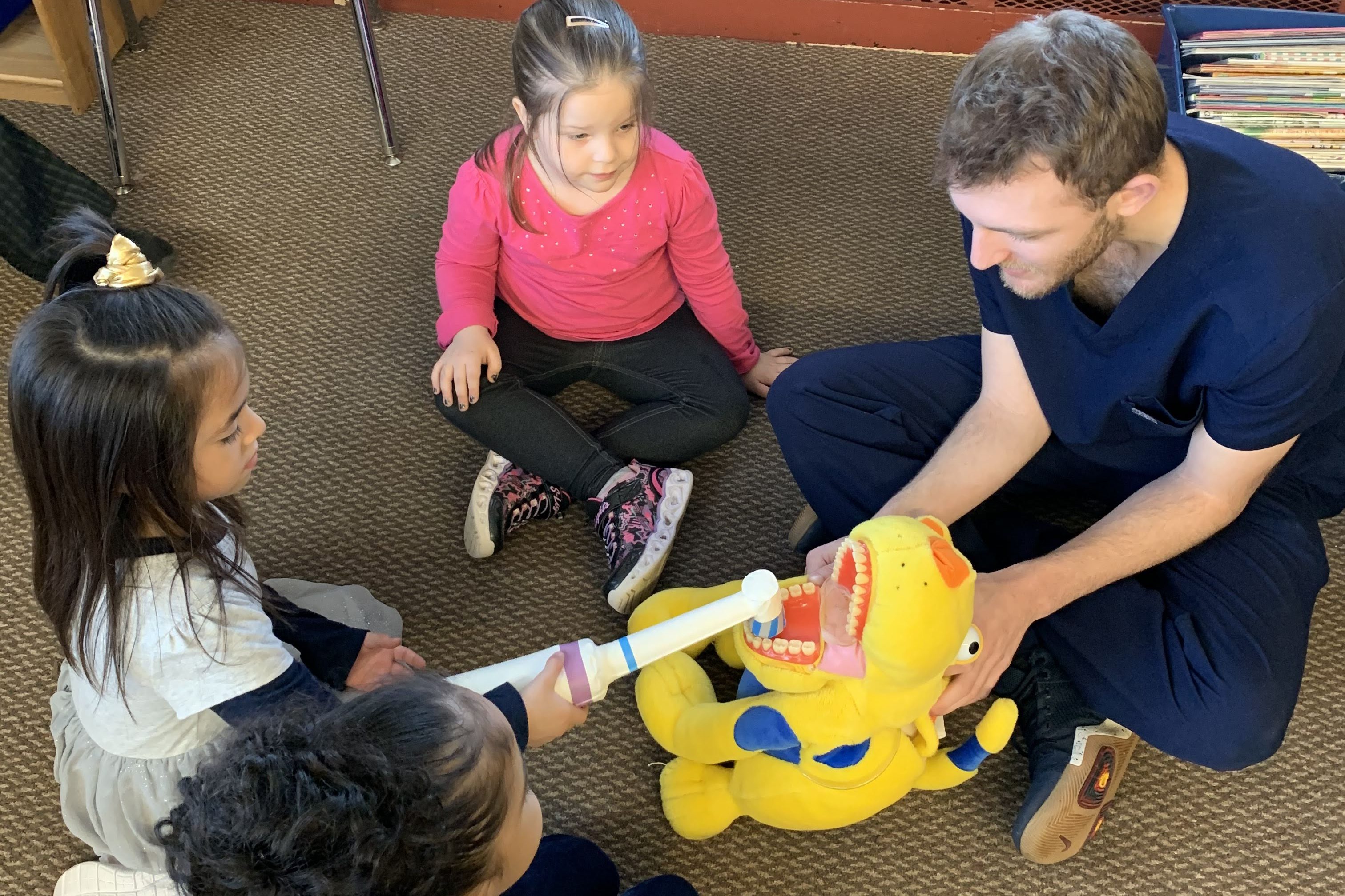 pre-K student brushes stuffed animal's teeth with a giant toothbrush