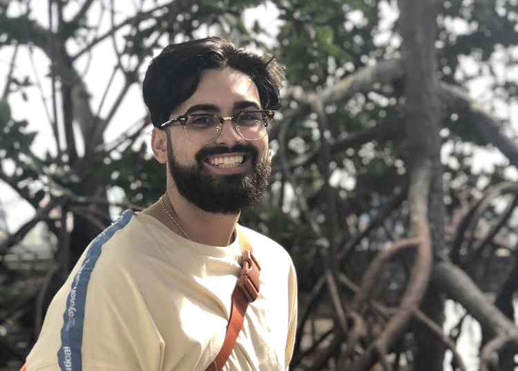 Caesar, a 2020 CLAS graduate, smiles outside on a sunny day.