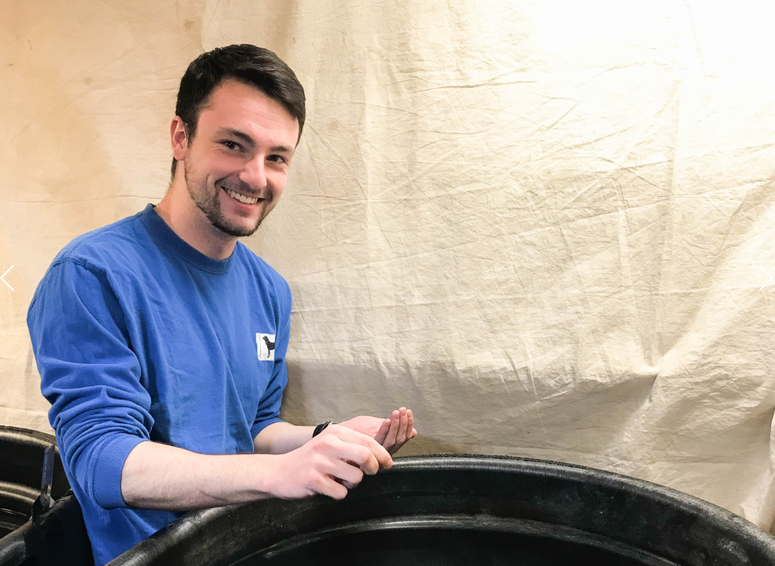 Student entrepreneur Peter Goggins poses near some barrels containing fish whose feed he is experimenting with.