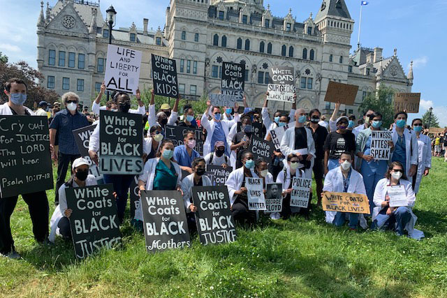 Demonstrators in white coats or scrubs and masks, Capitol in background