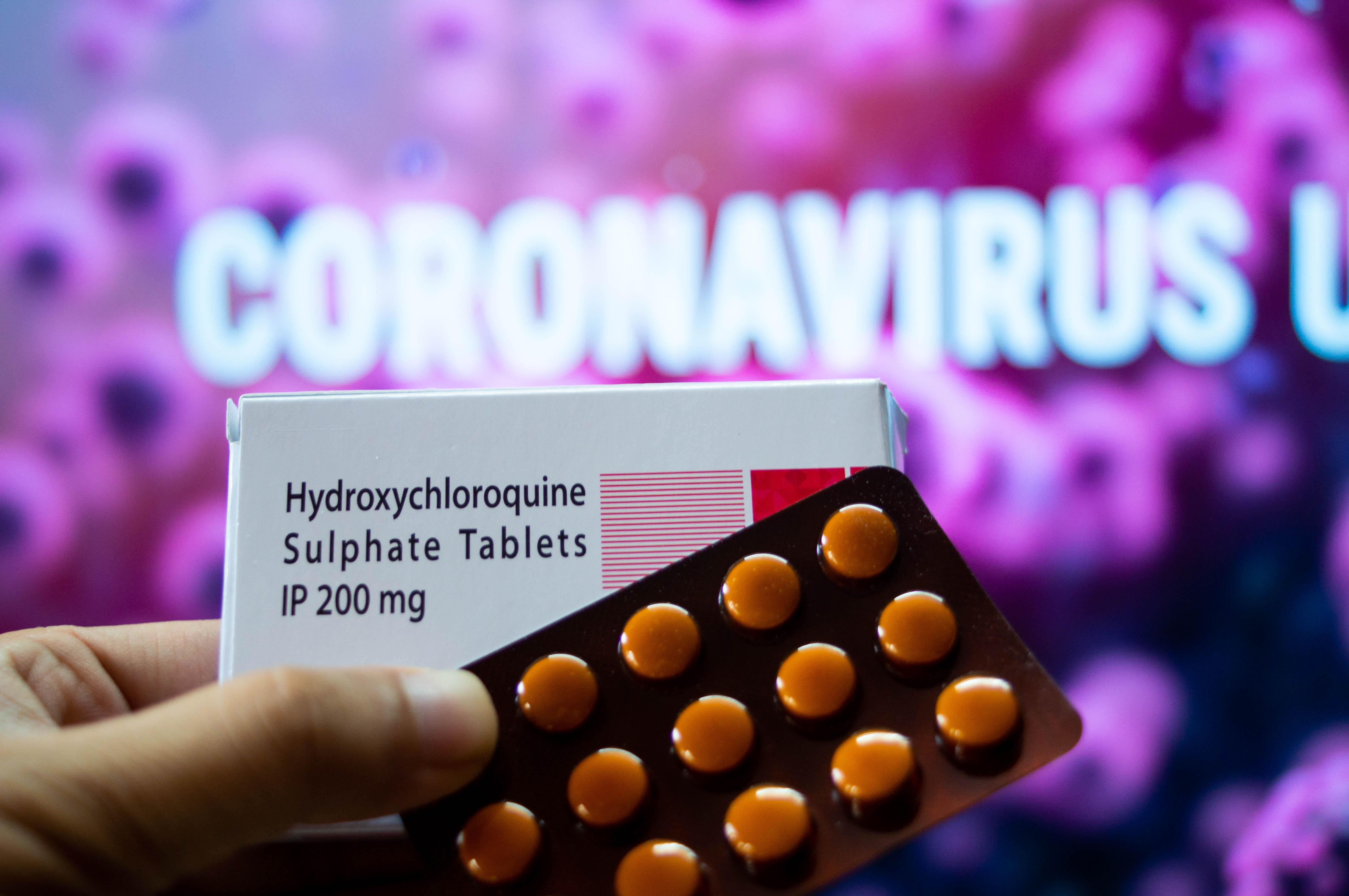 Photograph of hydroxychloroquine sulphate tables in a white coloured box in front of a red coloured board with coronavirus outbreak mentioned