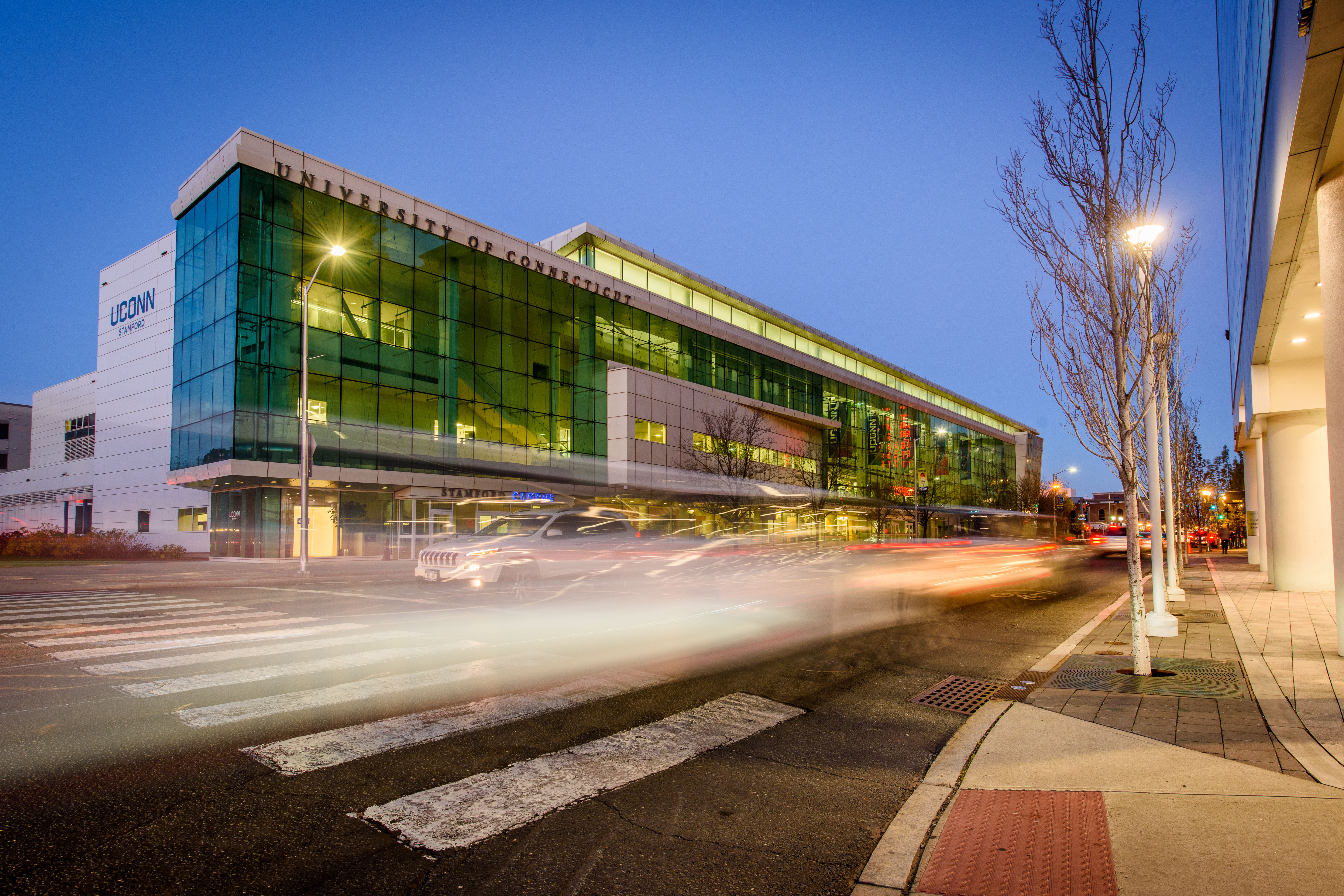 A picture of UConn Stamford at night, with cars driving by, leaving streaks of light behind them.