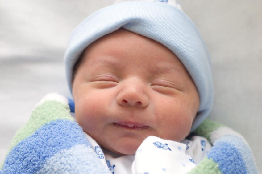 A newborn baby sleeps while wrapped in a blanket.