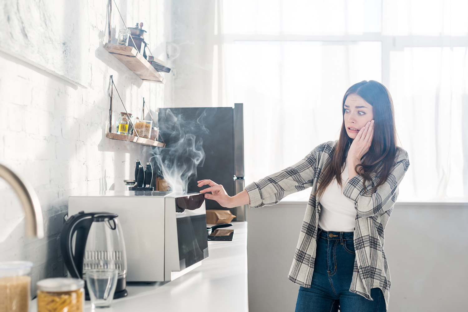 scared woman looking at broken microwave in kitchen