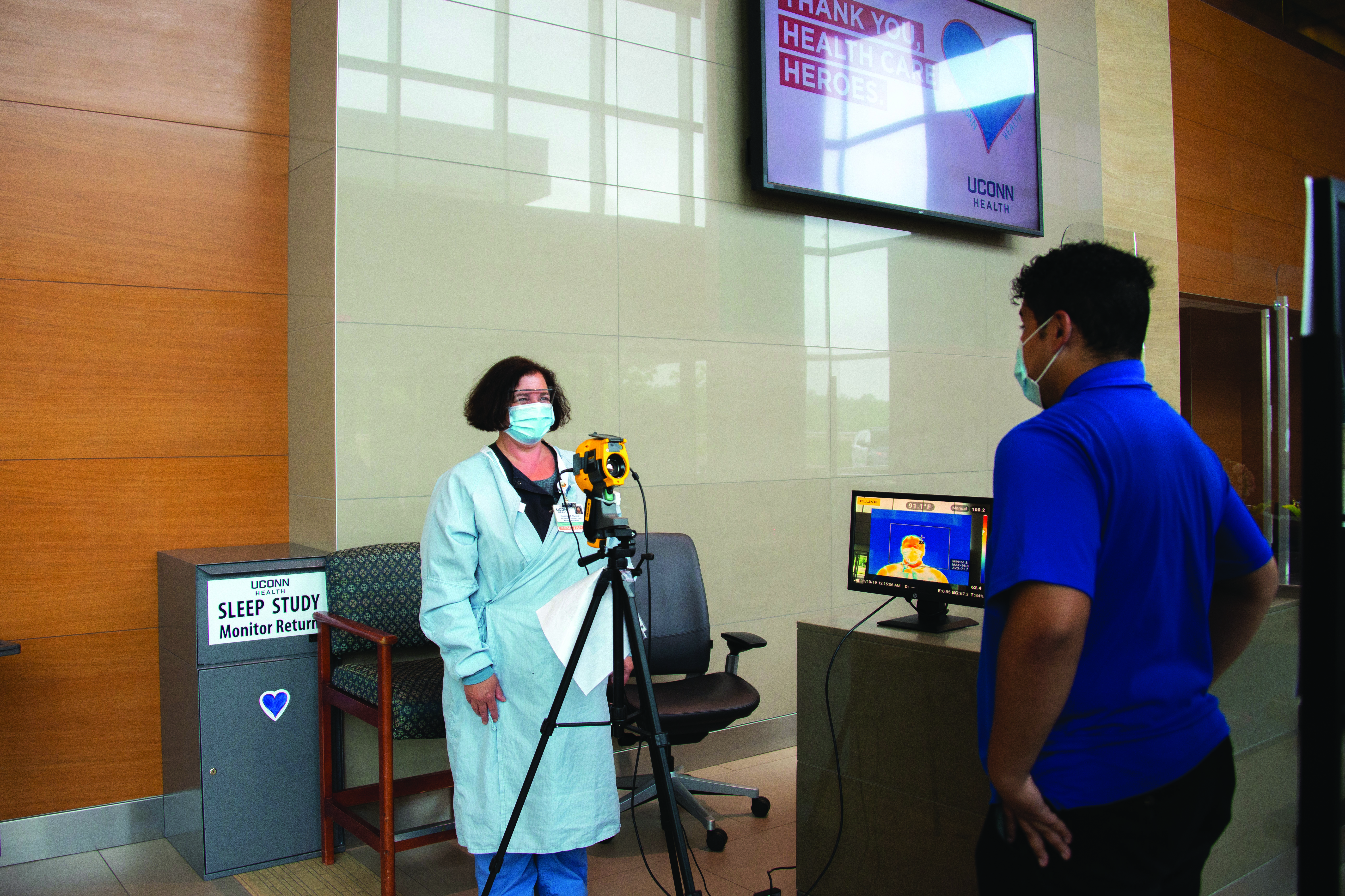 Medical assistant Regina Rushby takes William Cordero's temparature using a heat scanner, part of the screening process for entry at UConn Health. June 5, 2020 (Tina Encarnacion/UConn Health photo)