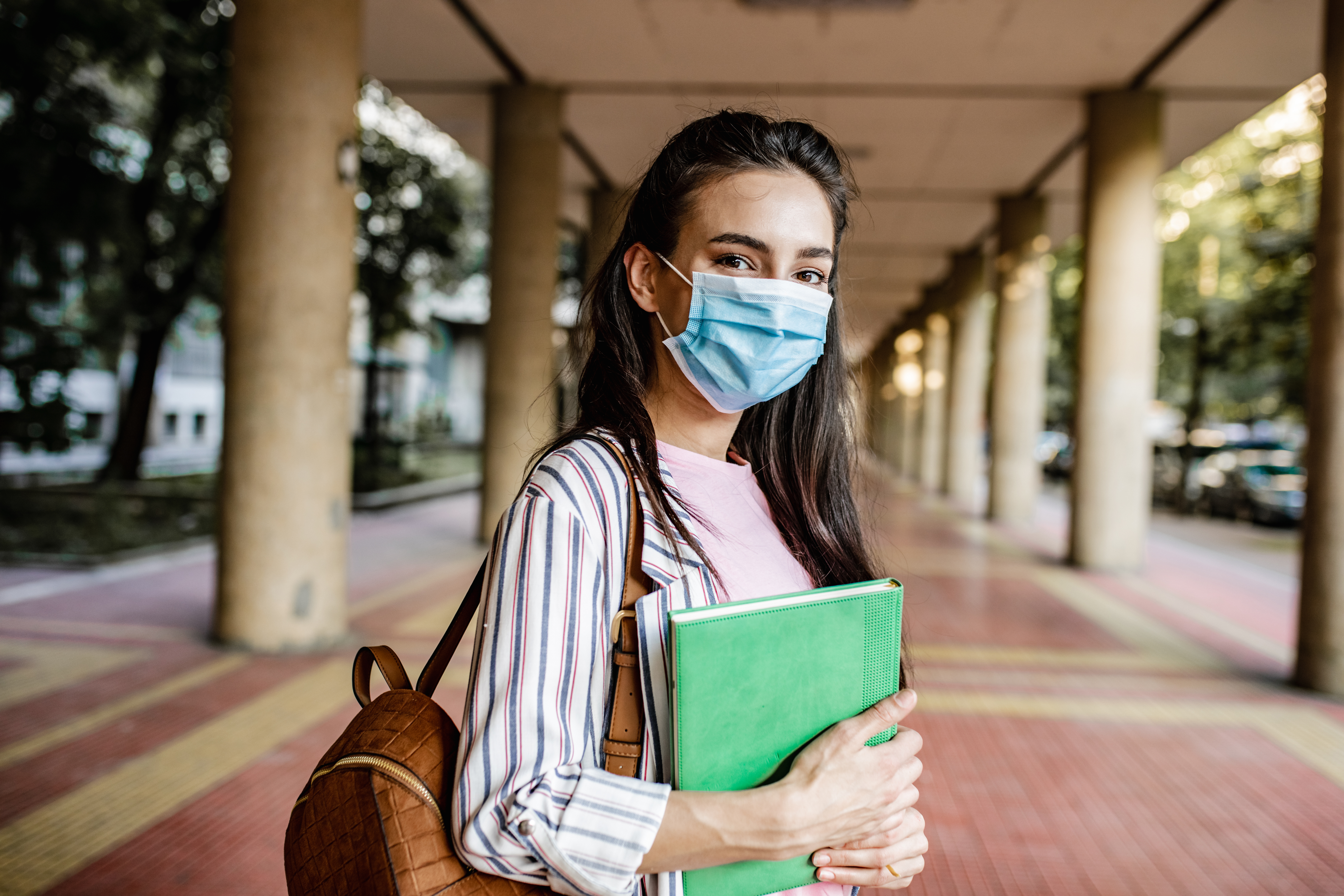 A young woman is holding a notebook and wearing a face mask