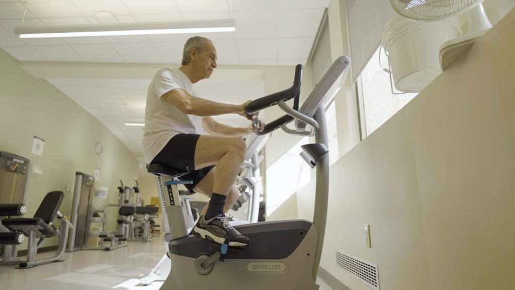 Bill Cateno riding an exercise bike under the direction of Dr. Moss.