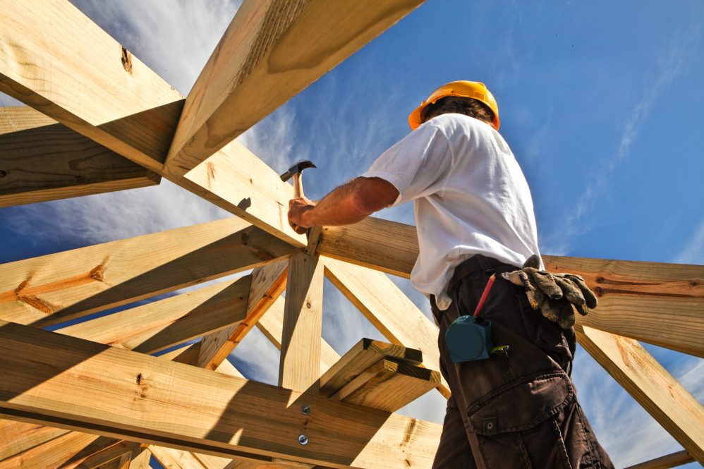 Man in hardhat using a hammer on a roof that he's building