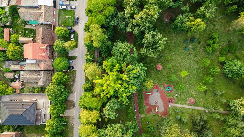 Aerial top view of spring park landscape with green trees, lawns and footpath. Park is surrounded by with houses.