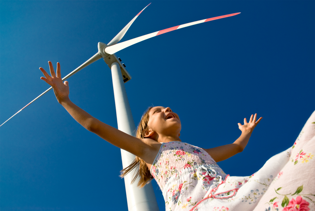 child playing with the wind near a wind turbine