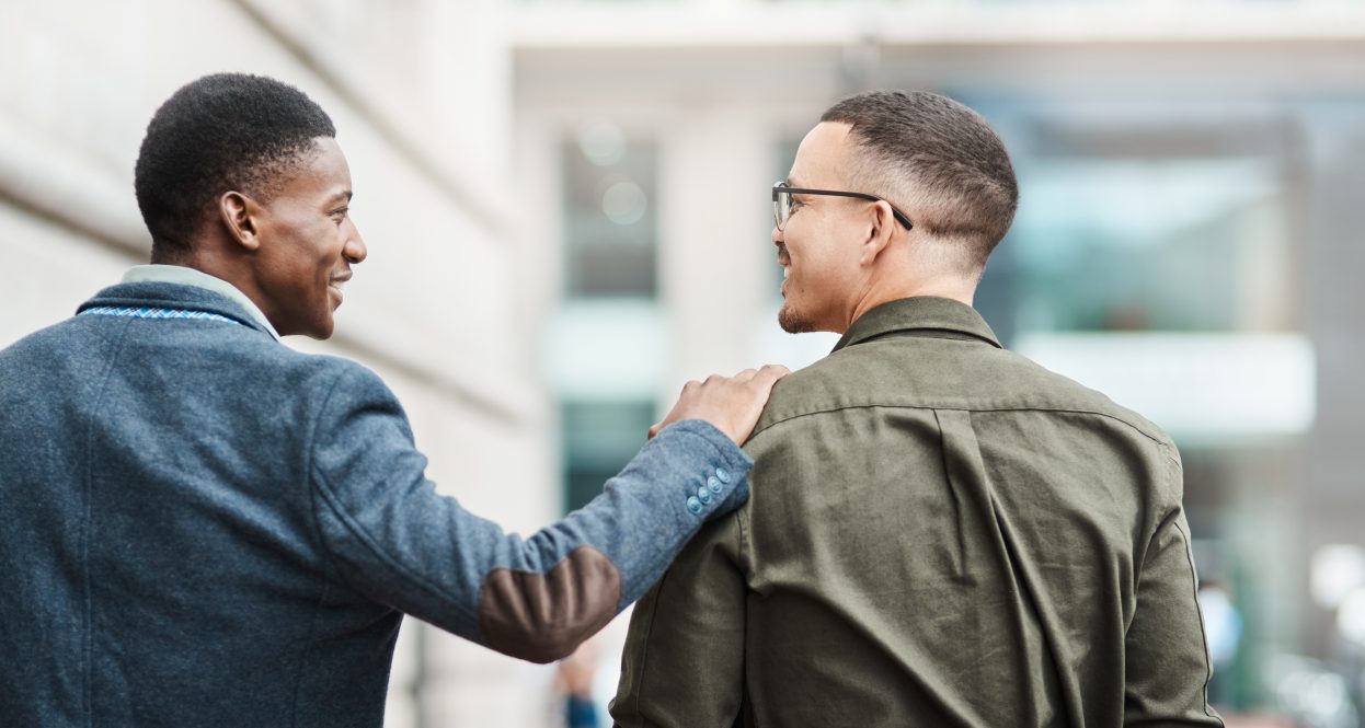 A young man puts his hand on the shoulder of a companion in a reassuring gesture.