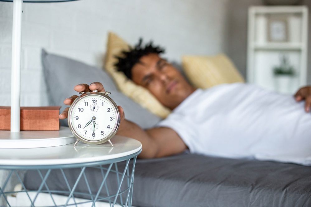 young African American man waking up and turning the alarm off