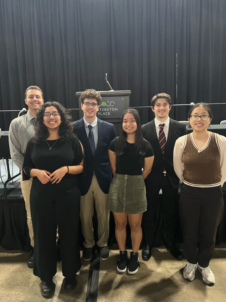 Six UConn students stand in front of a podium at the IMAT - Heat Treat conference wearing business clothing.