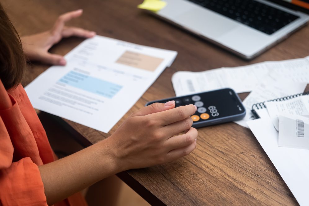 A Black woman calculates home heating costs with her calculator and laptop.