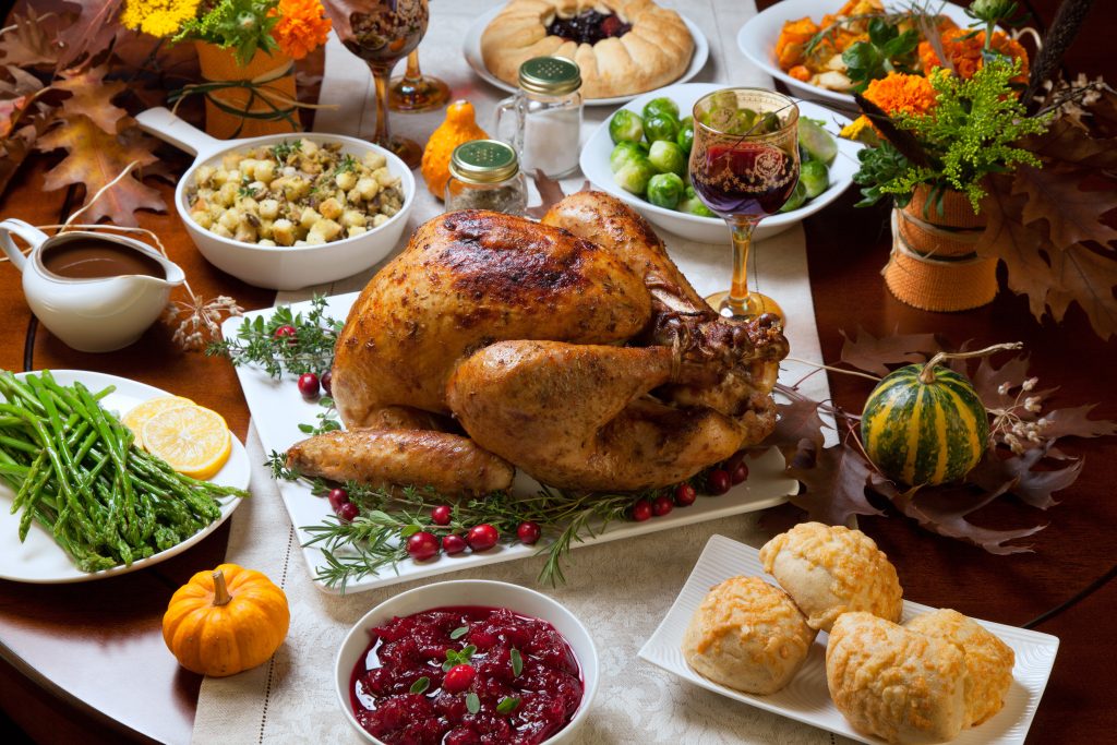 Roasted turkey garnished with cranberries on a rustic style table decoraded with pumpkins, gourds, asparagus, brussel sprouts, baked vegetables, pie, flowers, and candles.