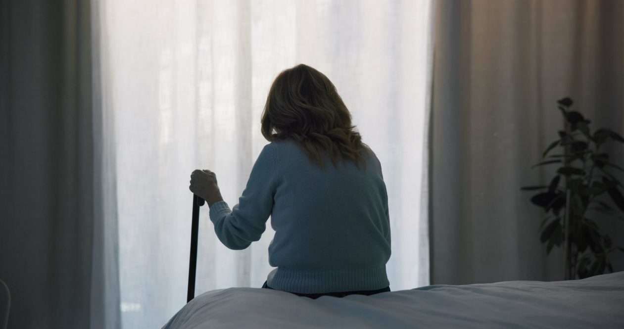 A woman, seen from behind, stares out the window of her room in a nursing home.