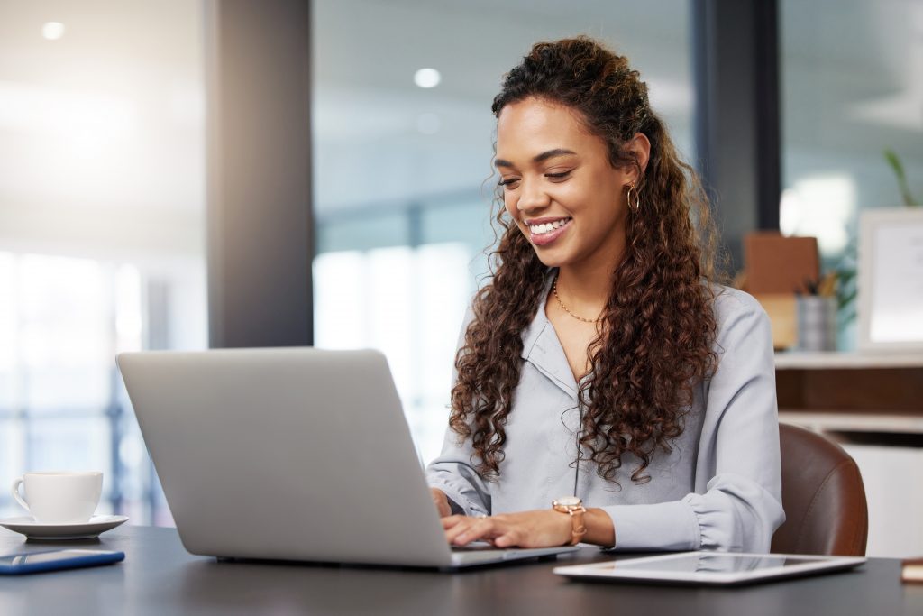 A woman in a public setting looks with determination at the open screen of a laptop computer.