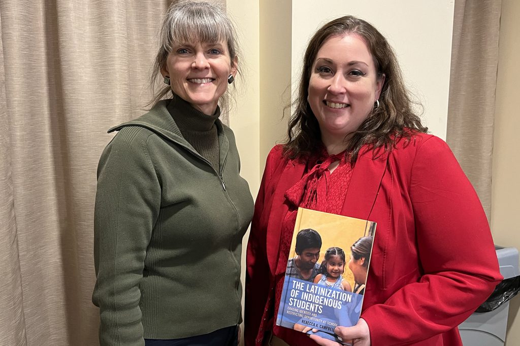 Two women, one holding a book, smile at the camera.