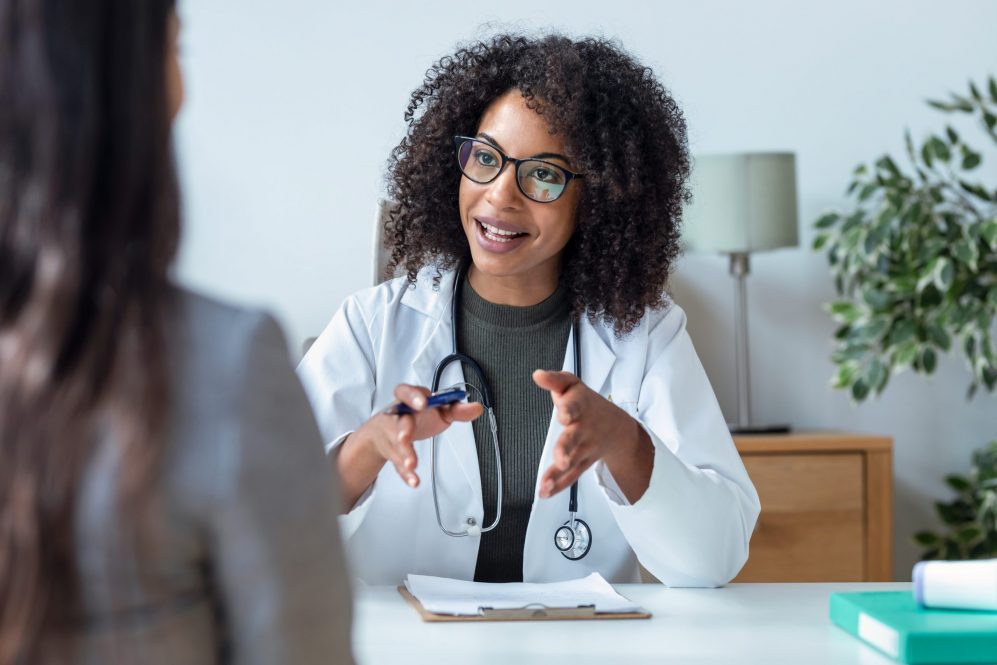 A doctor in a white lab coat speaks with a patient in her office.