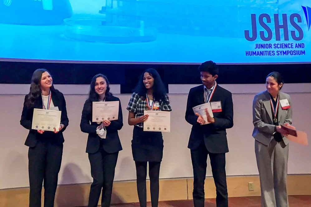 Five people holding certificates in front of projector screen