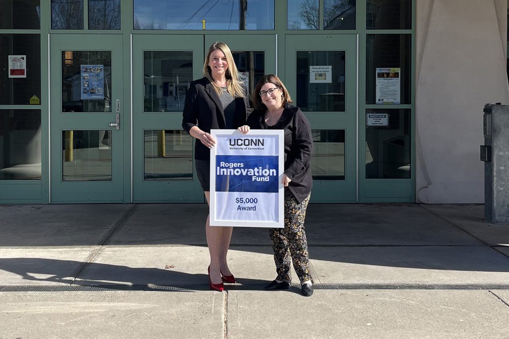 Two female educators, one tall and blonde and the other smaller and brown hair, hold a sign saying "Rogers Innovation Fund."