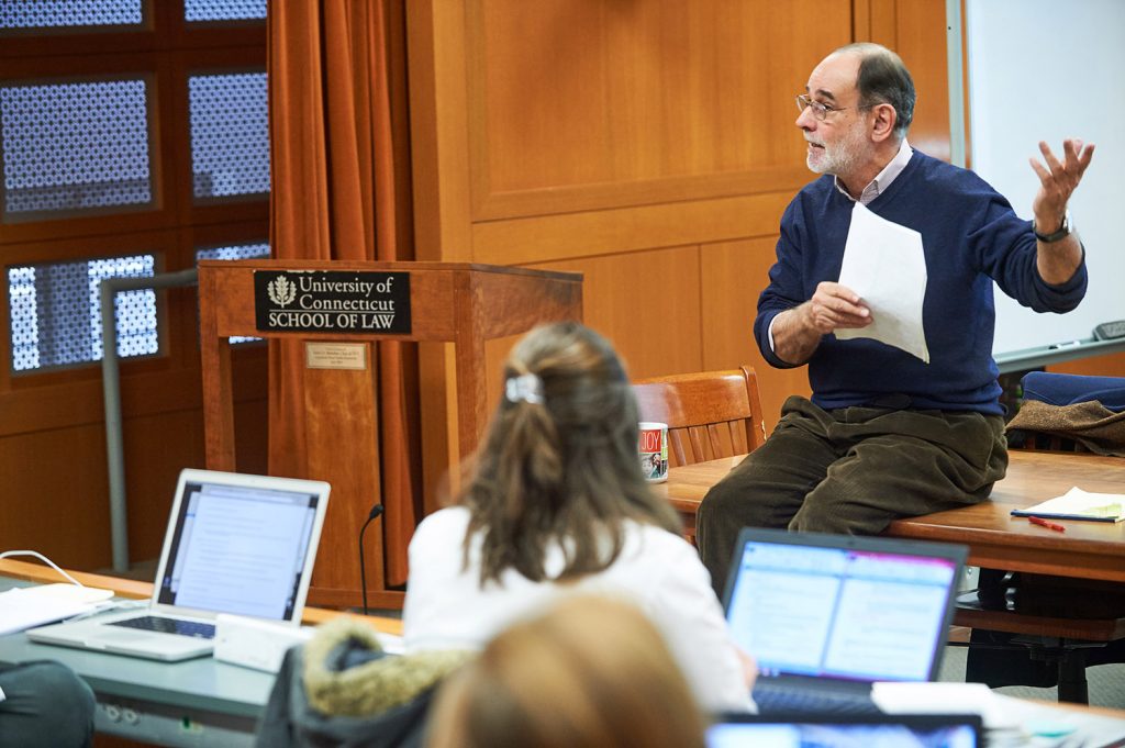 James Stark sits on a desk at the front of a classroom.