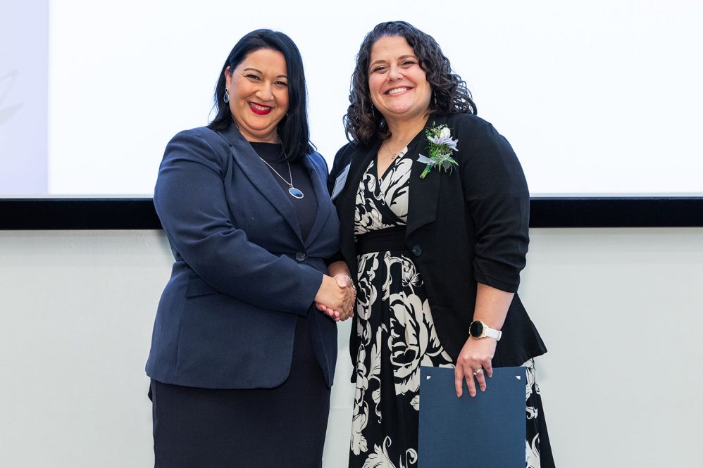 Two smiling professional females gather on stage at an awards event.