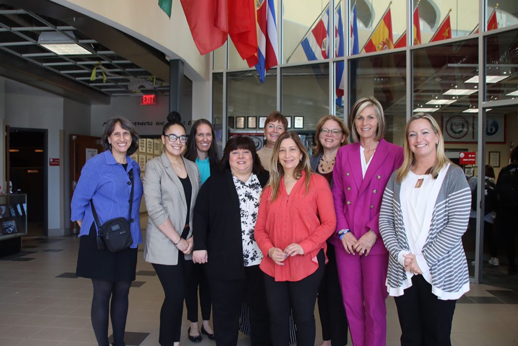 Nine women stand in a group and smile at the camera.