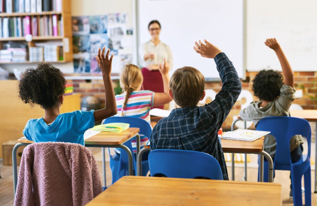 Students in an elementary school classroom raise their hands to be called on.