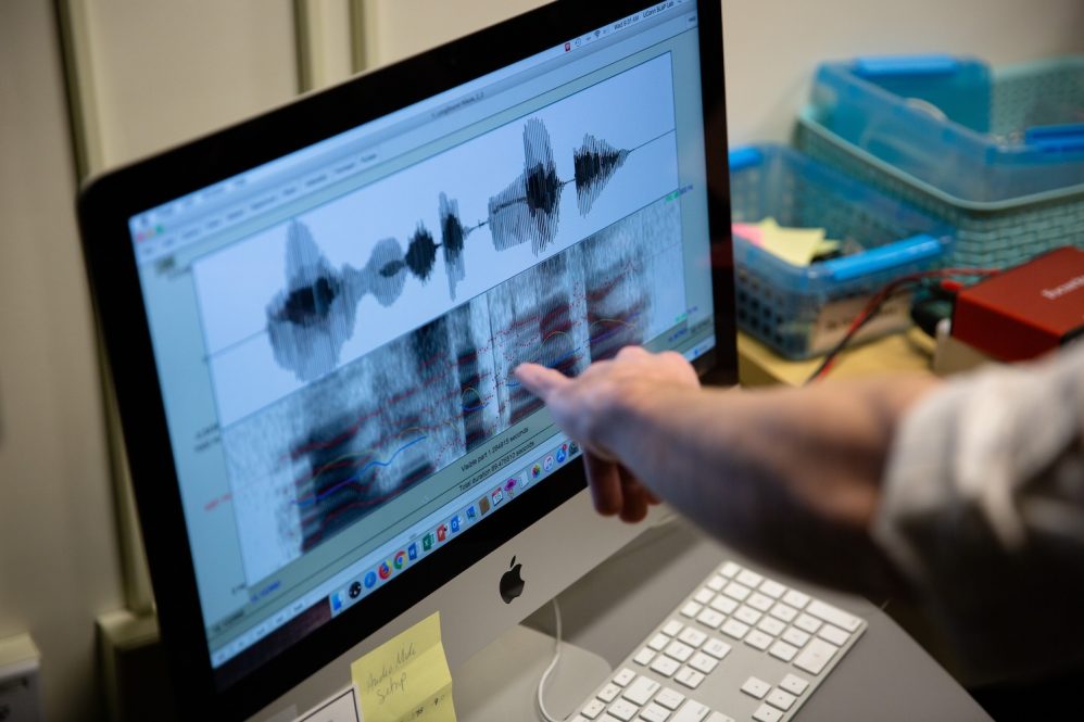 A hand pointing at a computer screen that has audio waves