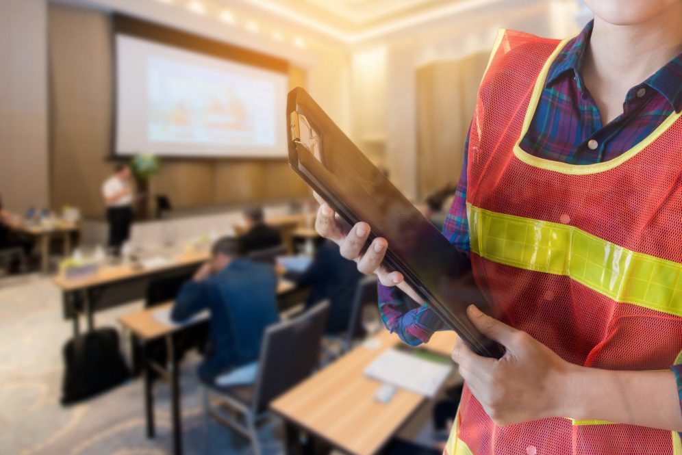 An occupational health and safety officer holds a clipboard in a seminar room.