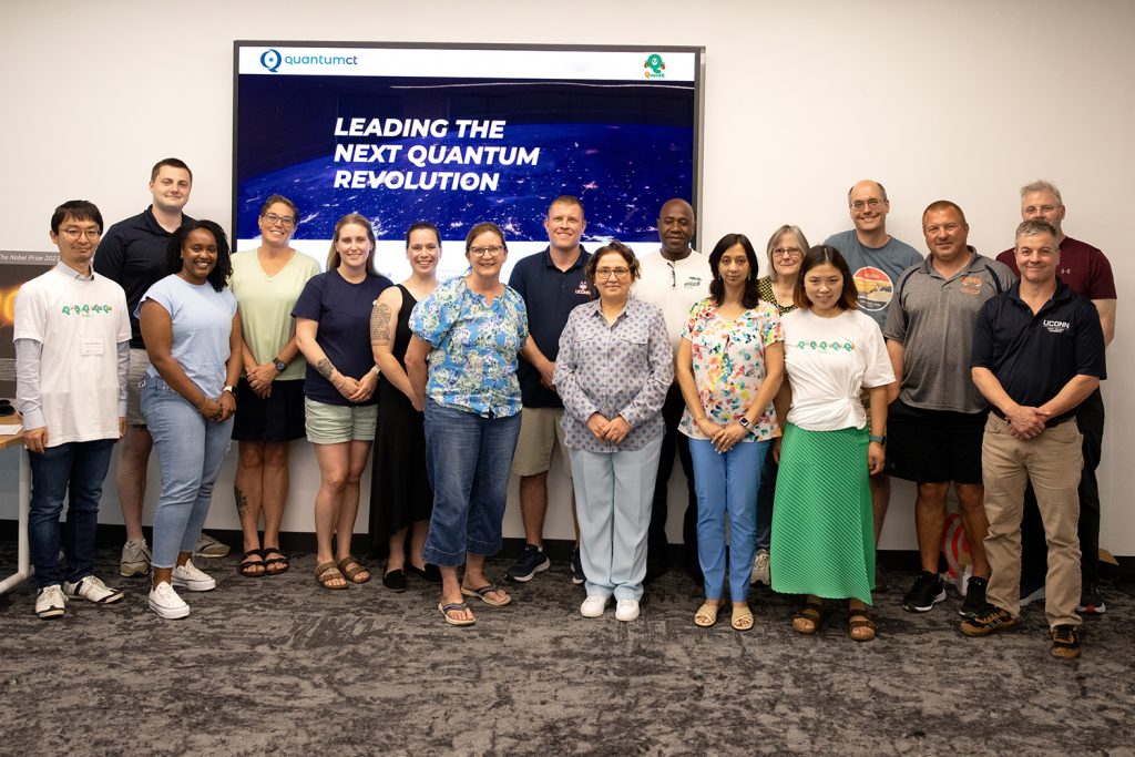 Five UConn faculty members and 12 local K-12 educators stand in front of a screen that reads "QuantumCT: Leading the next quantum revolution."