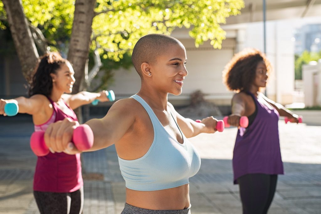 Group of three women using fitness weights outdoors.