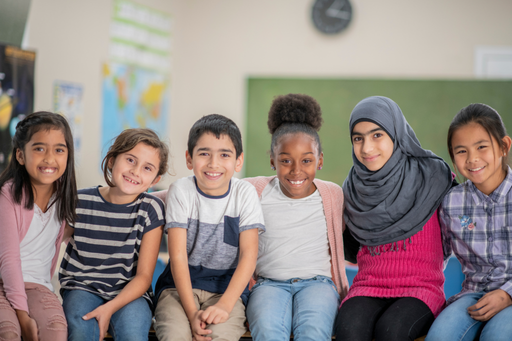 Six elementary age children sit in a row in a classroom.