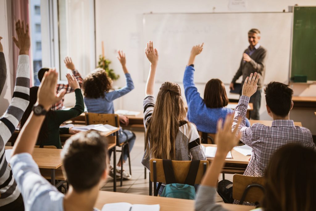 Back view of high school students raising hands on a class.